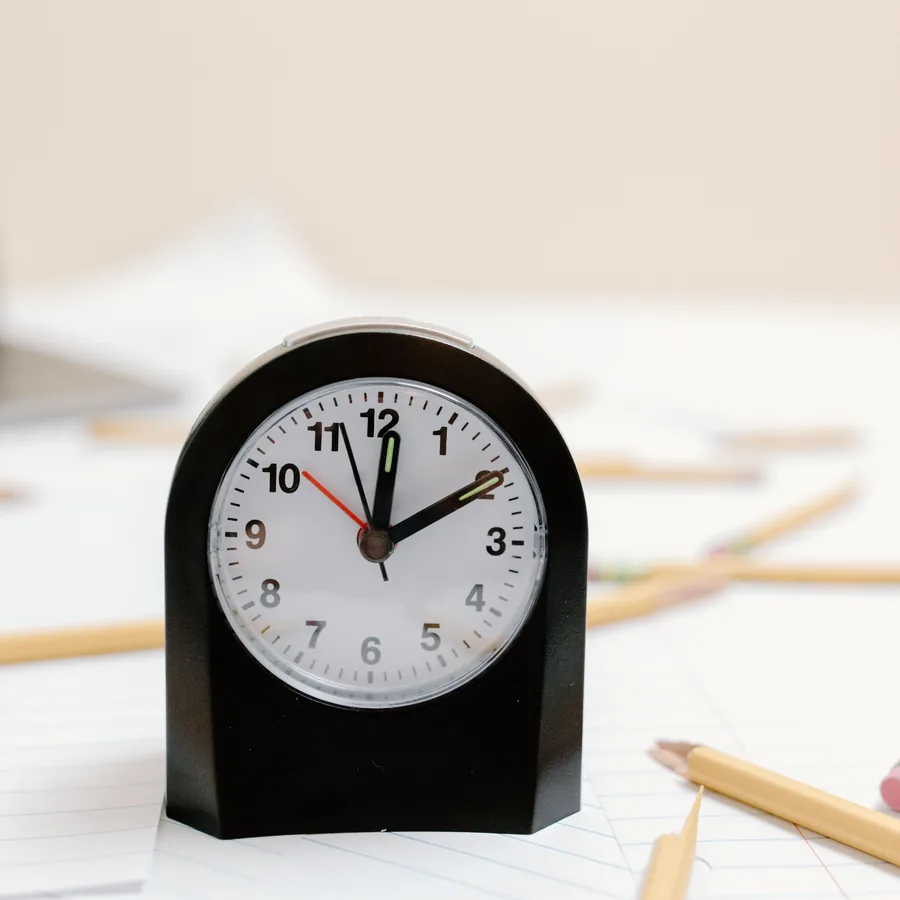Analogue clock on a desk beside pencils and paper