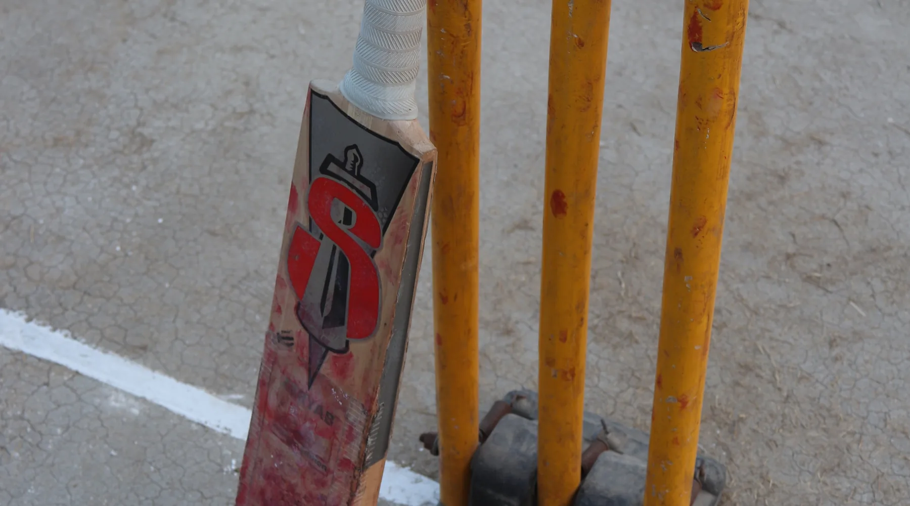 Cricket bat, red ball and wickets beside a pitch